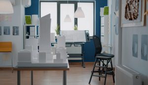 Empty technical office with real estate construction plan and building model on desk Empty technical office with real estate construction plan and building model on desk. Nobody in workplace used for construction design and architectural structure with urban project.